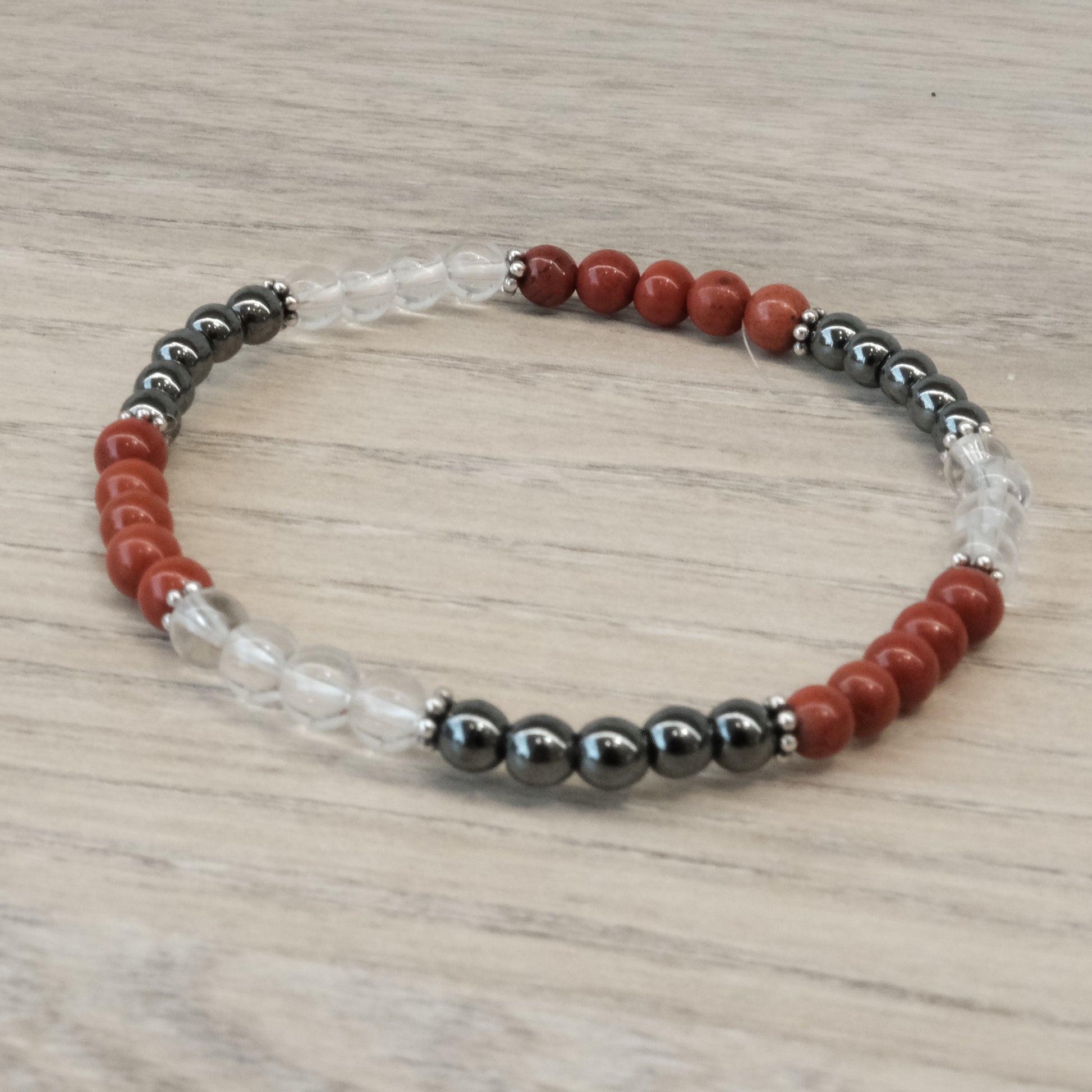 Energy and Vitality Bracelet with Red Jasper, Hematite, and Clear Quartz beads on a wood surface.