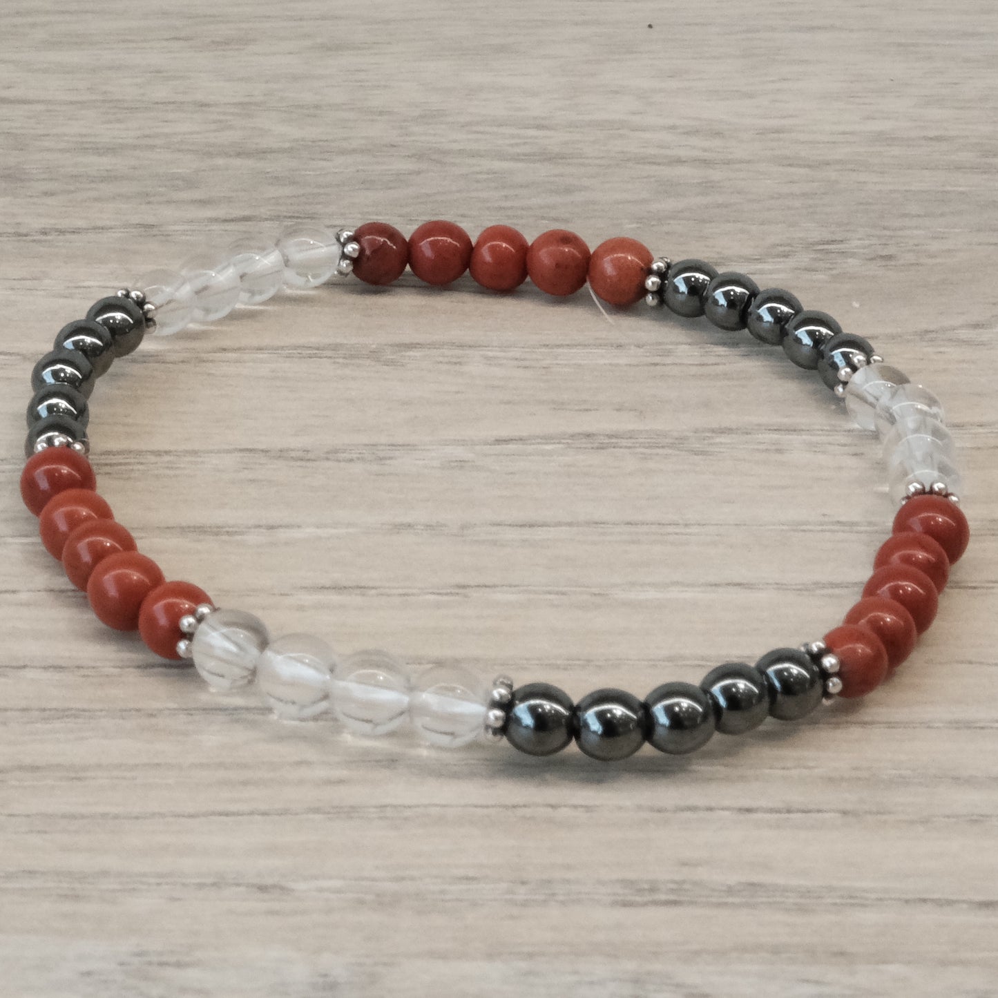 Energy and Vitality Bracelet 4MM with Red Jasper, Hematite, and Clear Quartz beads on a wooden background.