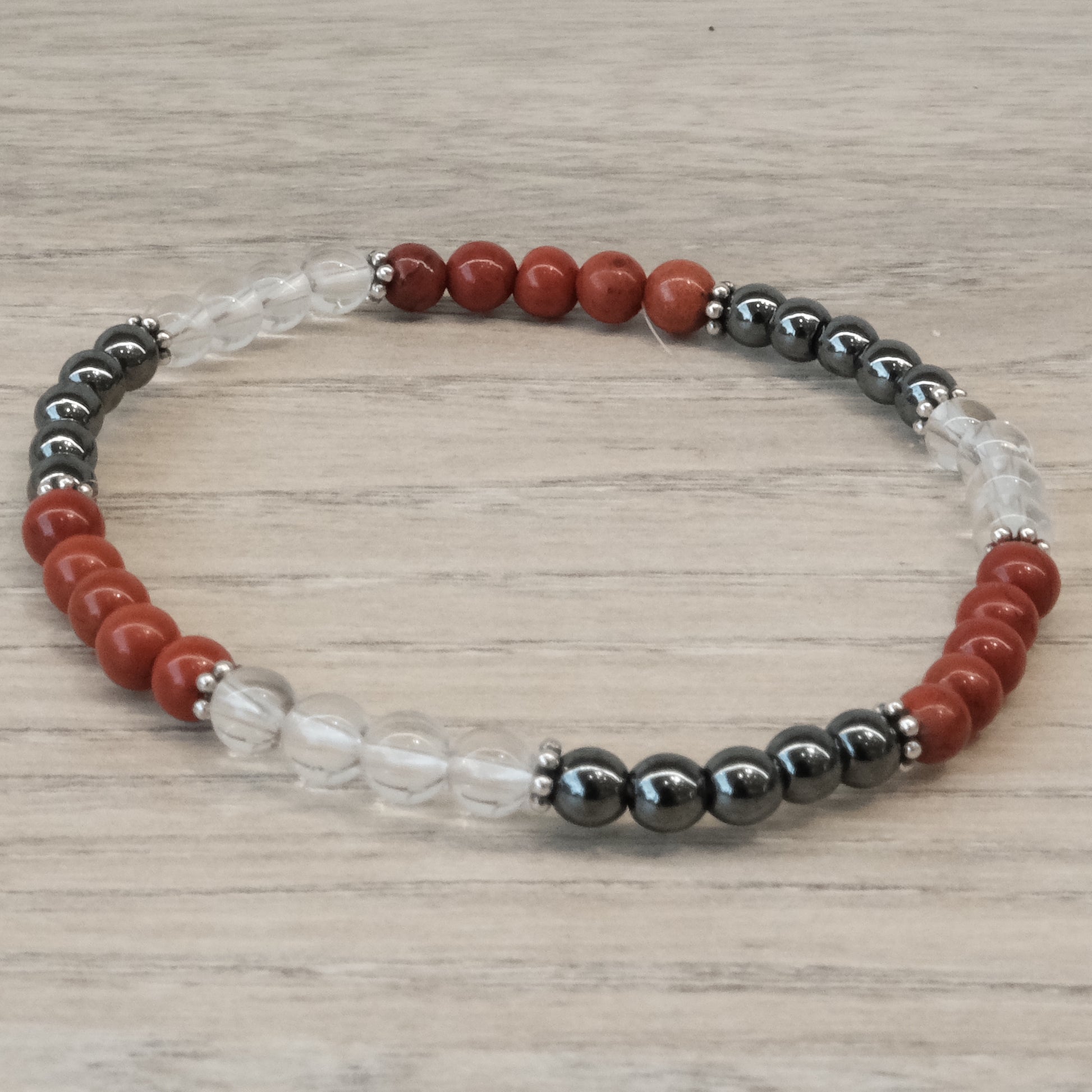 Energy and Vitality Bracelet 4MM with Red Jasper, Hematite, and Clear Quartz beads on a wooden background.