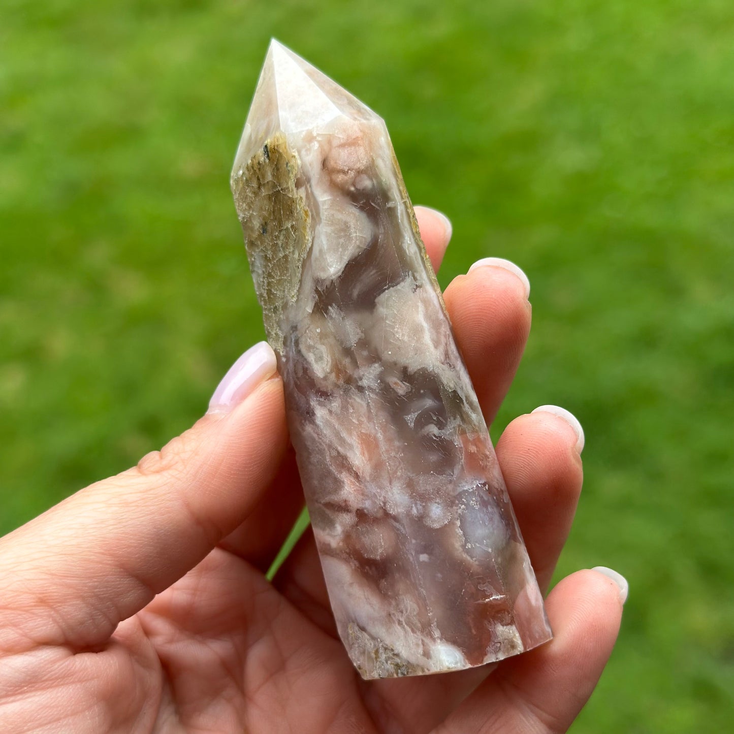 Hand holding Cherry Blossom Flower Agate Tower against a green background, showcasing its unique structure and natural hues.