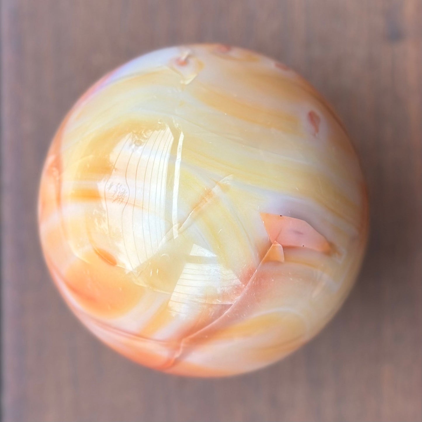 Carnelian sphere 3.5"D with reddish-orange and brownish-red swirls on wooden background.