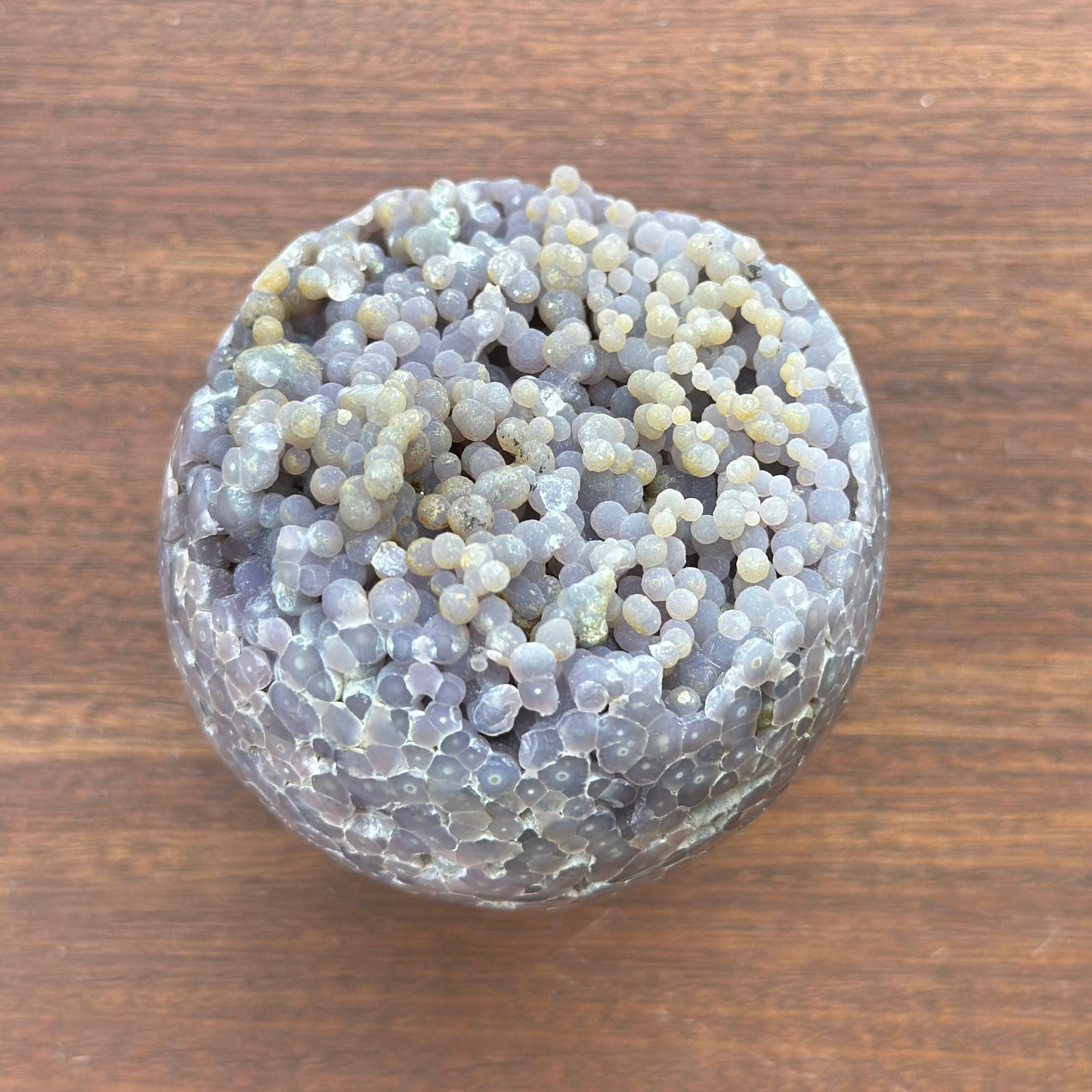 Grape agate sphere 243g gemstone with unique patterns on a wooden surface, promoting stability and emotional balance.