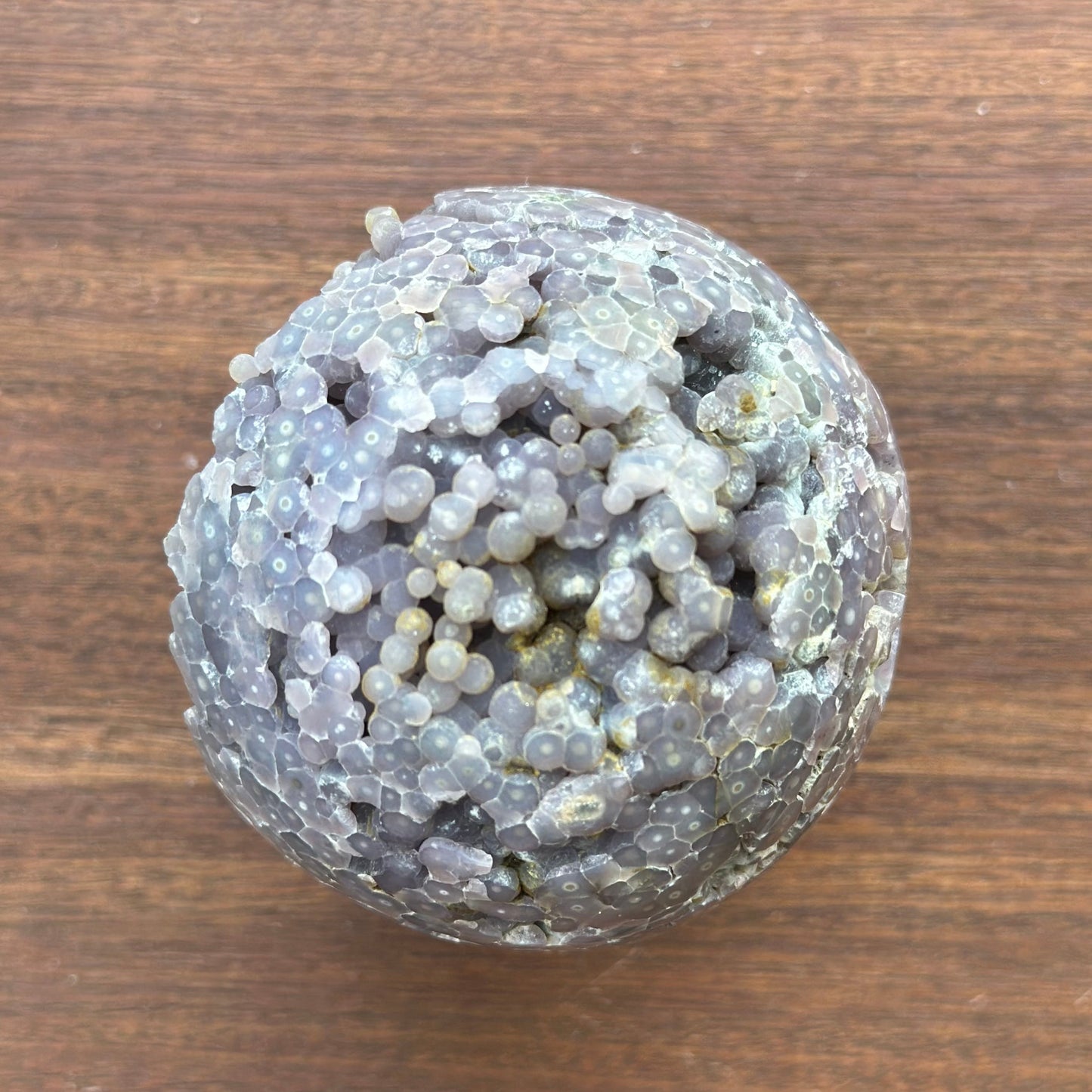 Grape agate sphere 243g with unique texture, promotes inner stability and calmness, displayed on wooden surface.