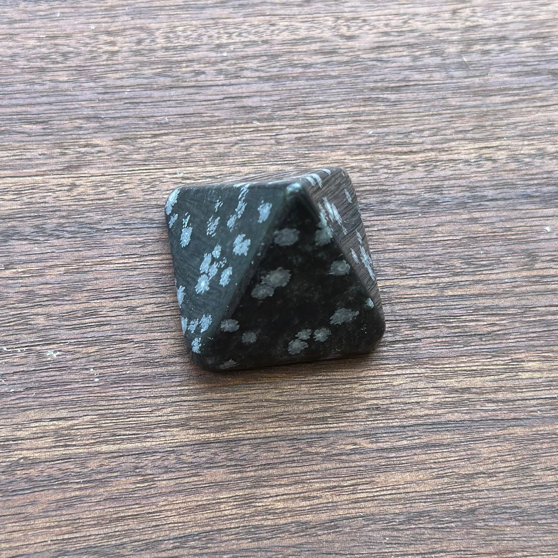 Snowflake Obsidian pyramid on wooden surface, promoting healing and inner clarity through meditation.