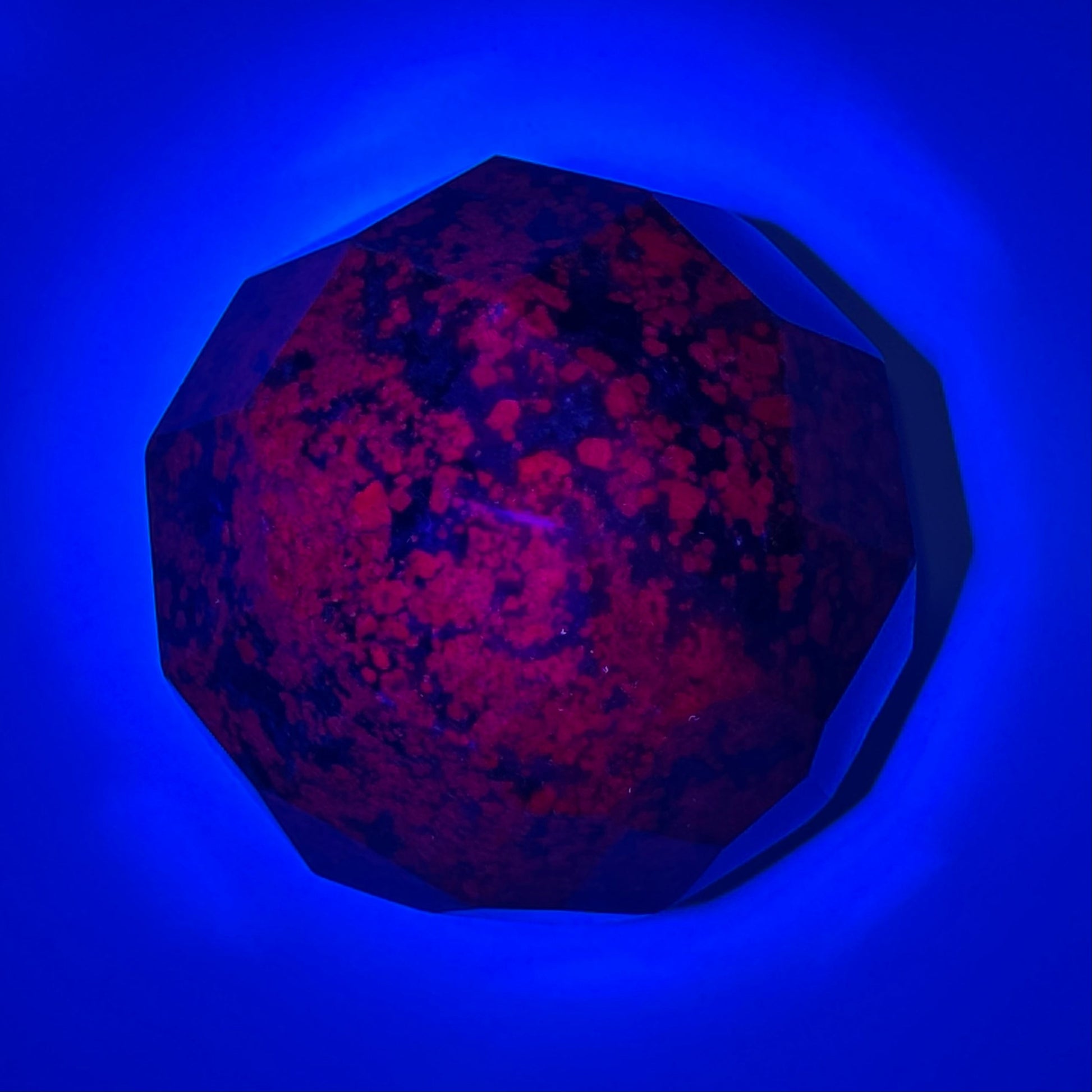 Ruby kyanite faceted sphere displaying vibrant red hues on a blue background, symbolizing love and energy.