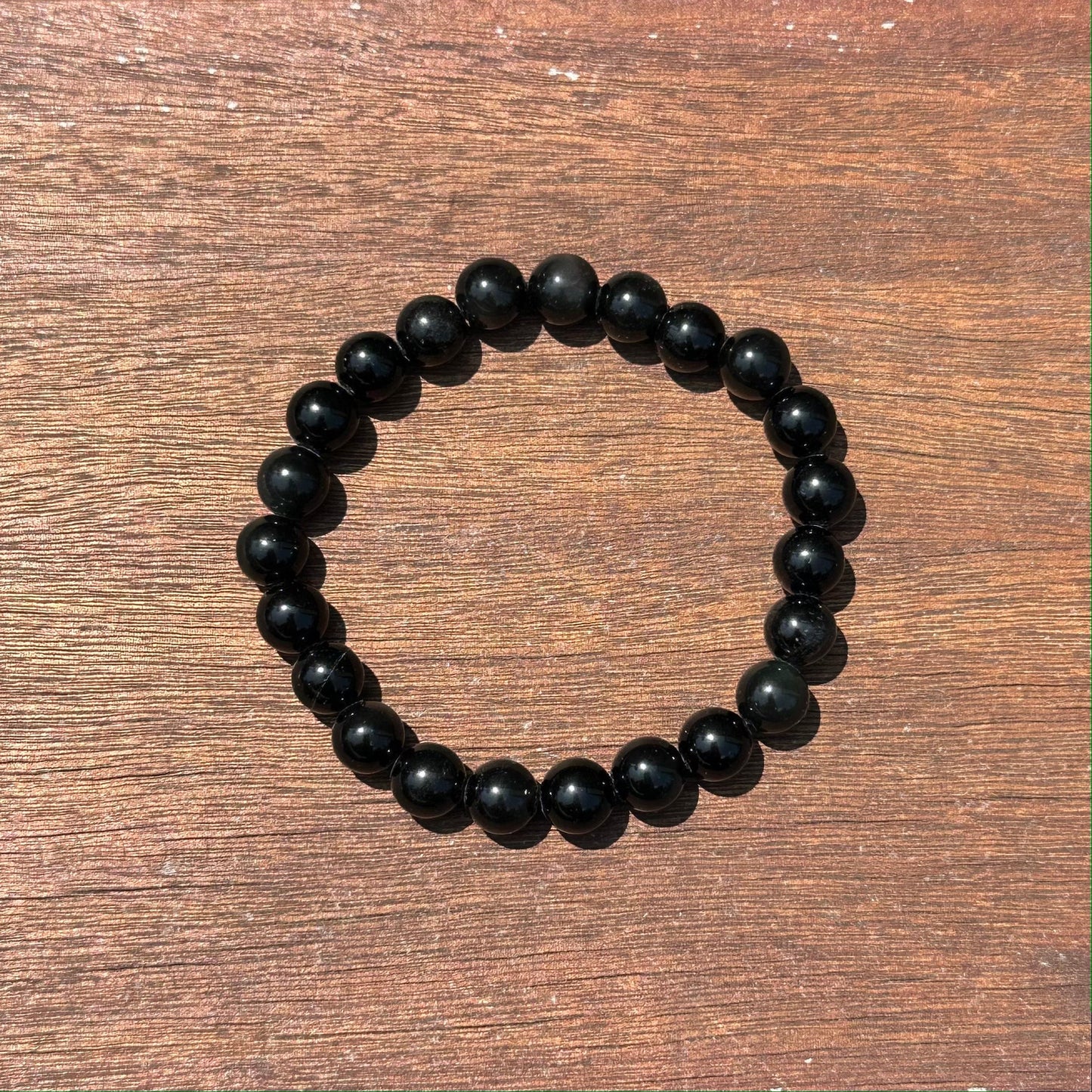 Rainbow Obsidian bracelet featuring 8mm beads, elegantly displayed on a wooden surface. Perfect for style and healing.