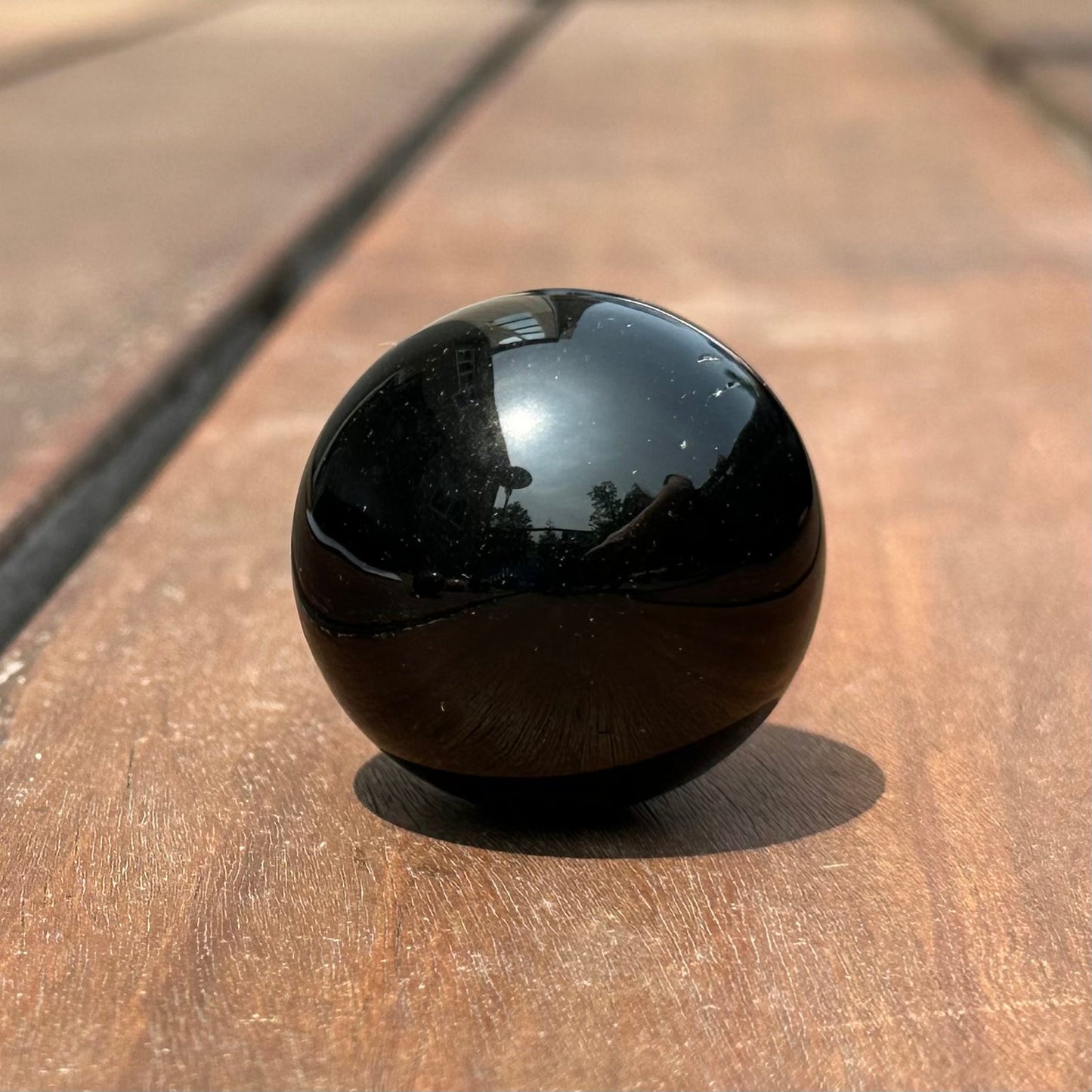 Black obsidian sphere on wooden surface, 1.25" diameter, known for protection and stress relief.