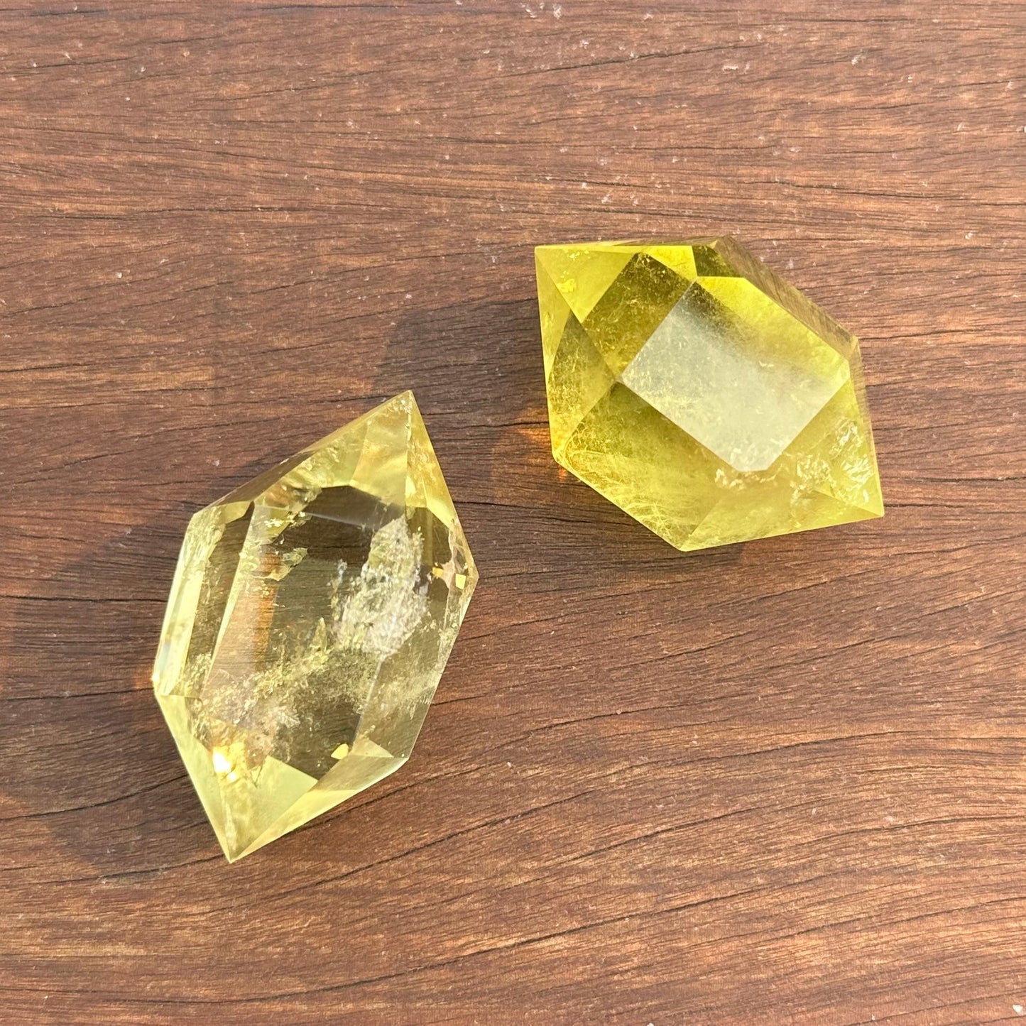 Two citrine double terminated points showcasing their vibrant yellow color and natural facets on a wooden surface.