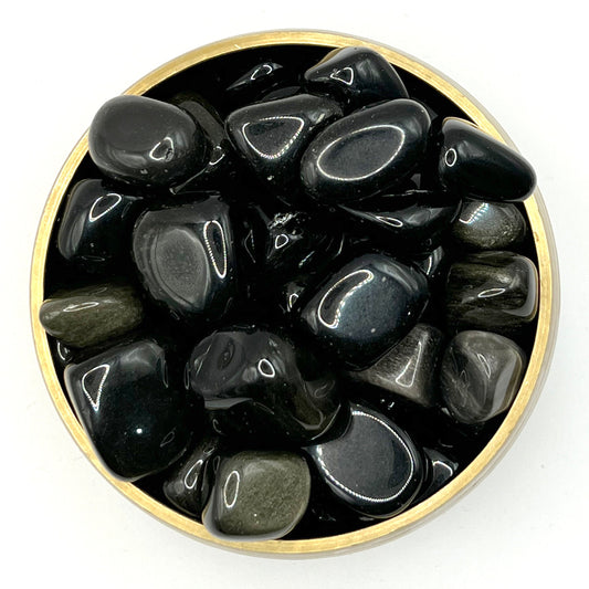Tumbled golden sheen obsidian stones in a round gold bowl, showcasing their glass-like surface and shimmering effect.