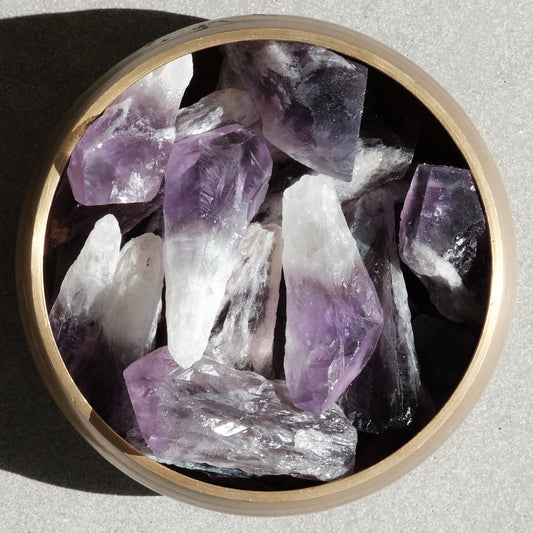 Raw amethyst crystals in a wooden bowl, showcasing natural purple hues and textures, known for their calming and healing properties.