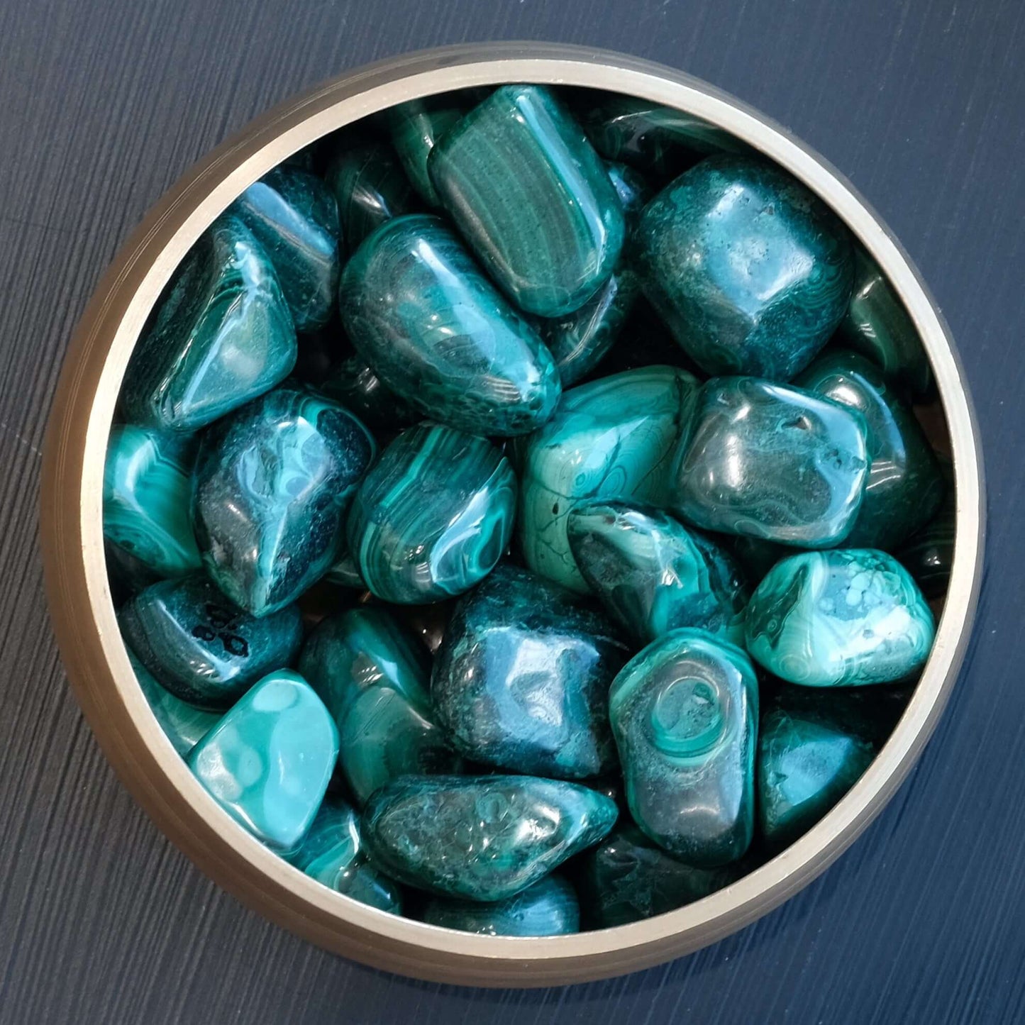 Malachite tumbled stones 10-20MM in a round container, showcasing their rich green colors and unique patterns.