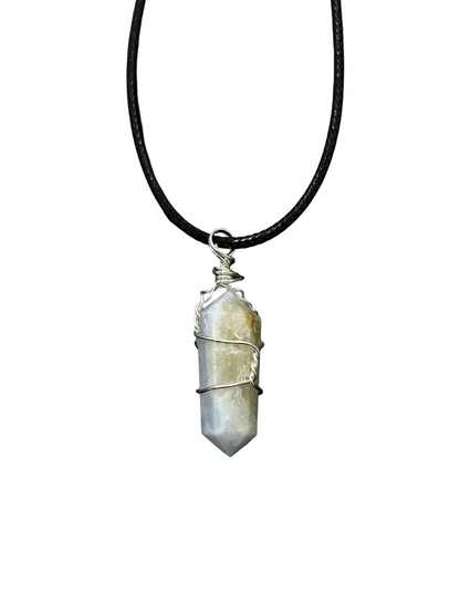A raw blue lace agate crystal pendant necklace wrapped in silver wire, hanging from a black cord against a dark gray textured background.