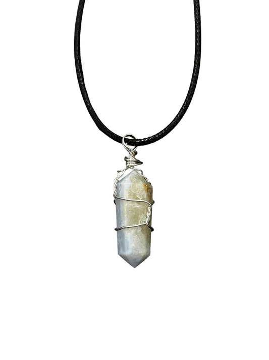 A raw blue lace agate crystal pendant necklace wrapped in silver wire, hanging from a black cord against a dark gray textured background.