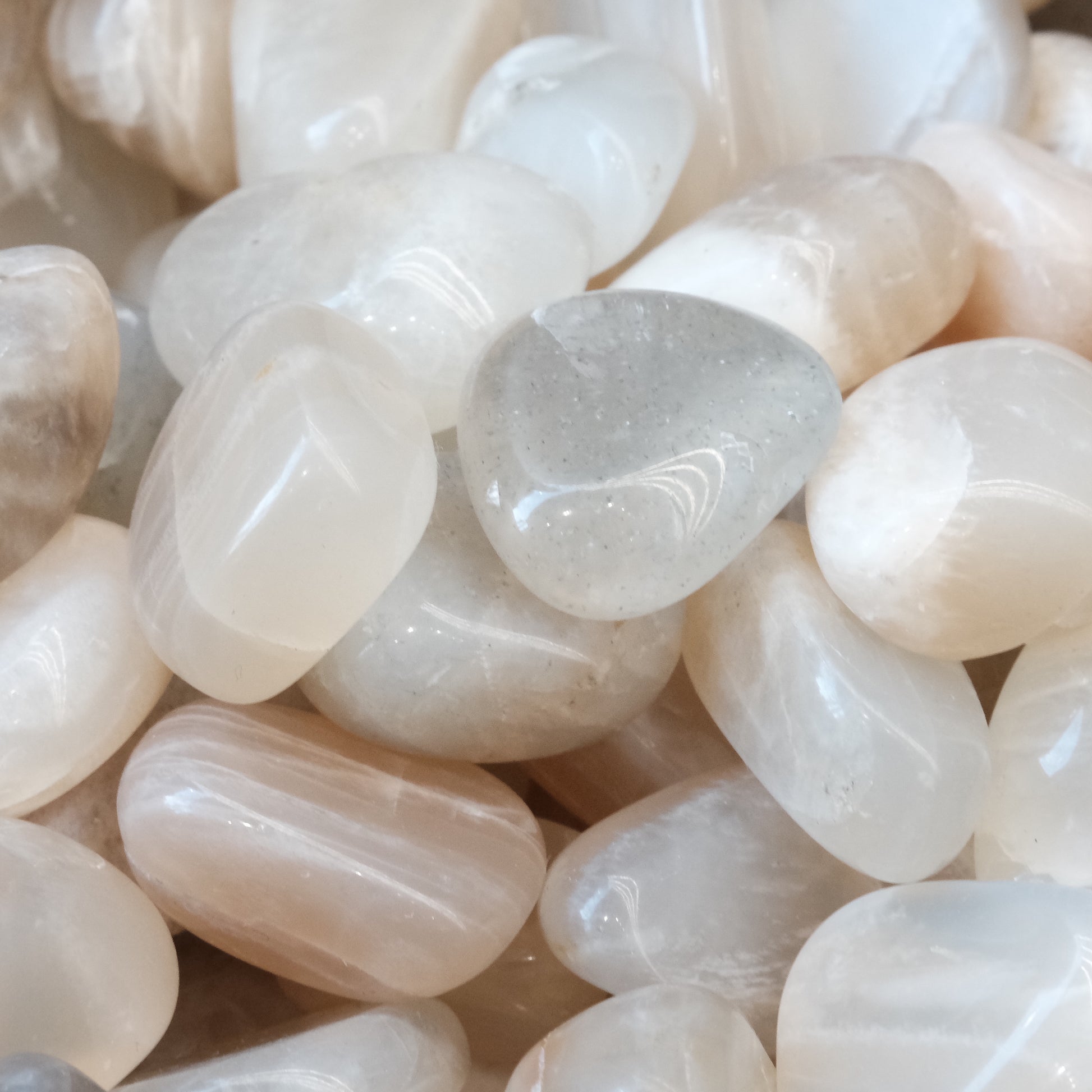 Smooth white moonstone tumbled stones, known for promoting inner strength, serenity, and enhancing intuition and creativity.