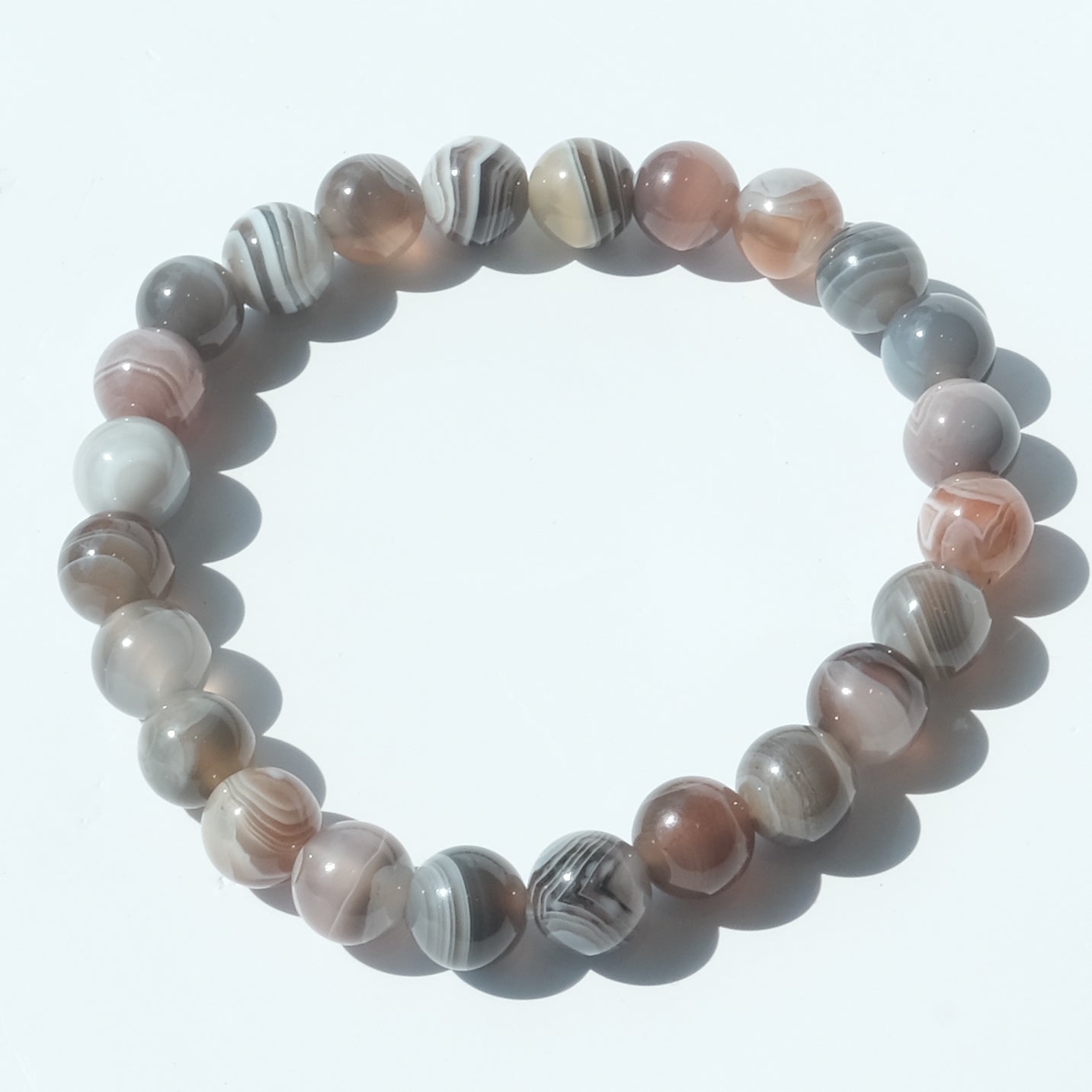 A beaded stretch bracelet made of polished round agate-like beads in shades of pink, gray, white, and brown with natural banding patterns, arranged in a circle on a white background.