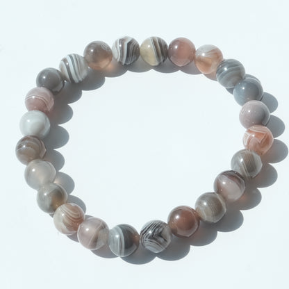 A beaded stretch bracelet made of polished round agate-like beads in shades of pink, gray, white, and brown with natural banding patterns, arranged in a circle on a white background.