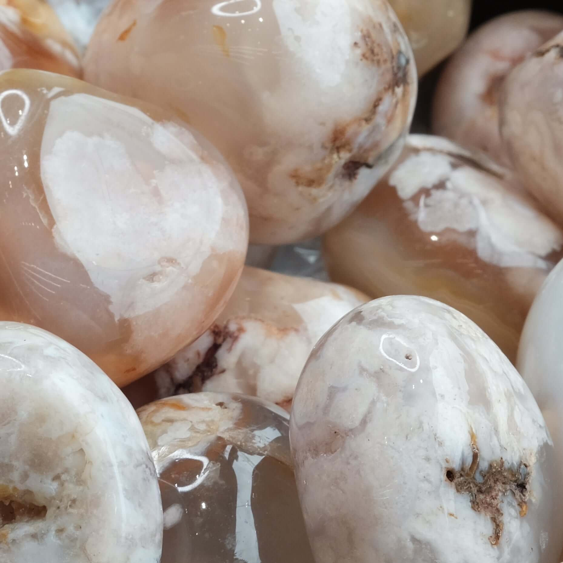 Tumbled flower agate stones with light pink hues and delicate inclusions, known for healing properties and promoting relaxation.