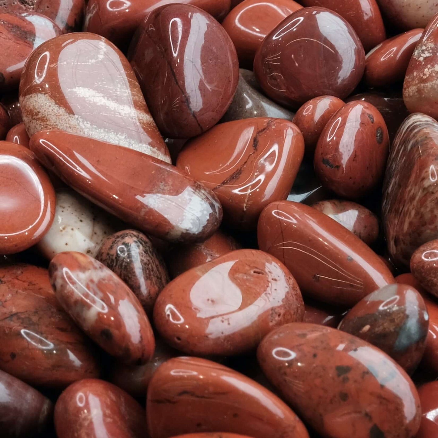 Smooth red jasper tumbled stones, showcasing glossy surfaces and rich earthy tones, known for grounding and protective properties.