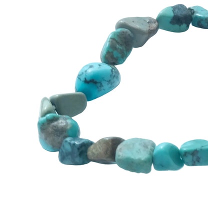 A close-up of a beaded necklace made of irregular turquoise-blue and gray natural stone beads on a light blue background.