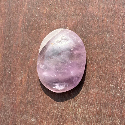 Amethyst worry stone on wooden surface, promotes stress relief, mood stabilization, immune support, and spirituality enhancement.